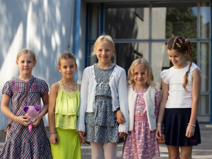 Päť usmiatych dievčat stojí vedľa seba pred vchodom do školskej budovy