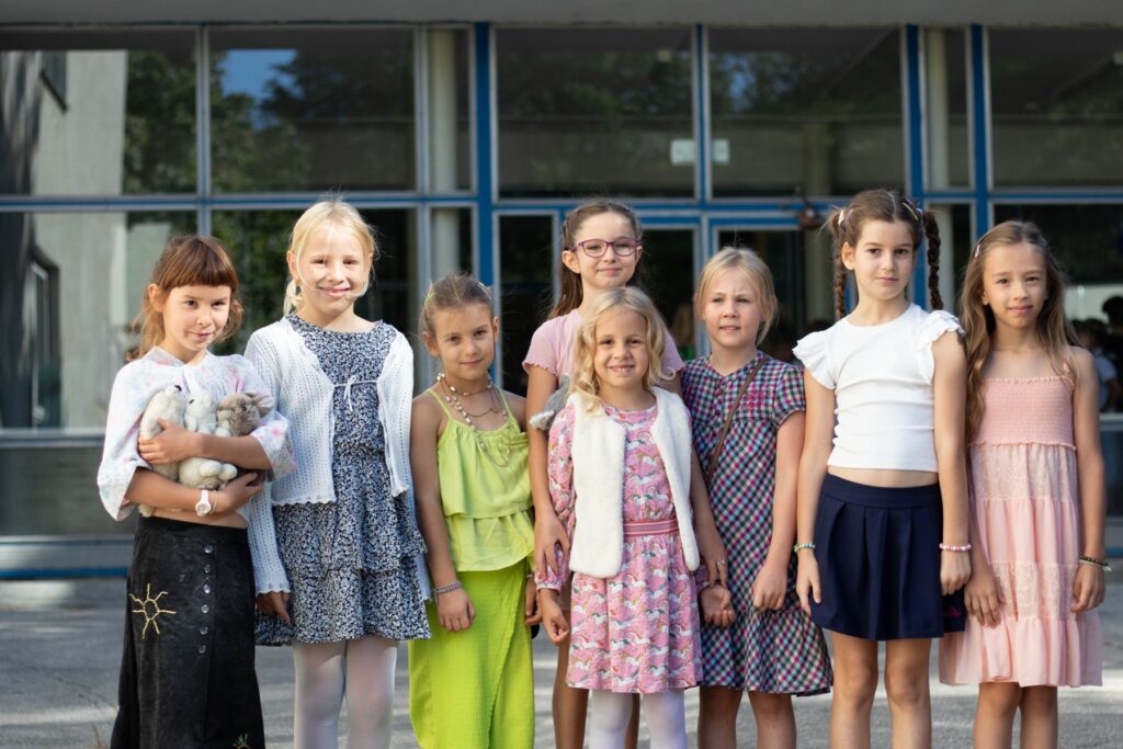 Skupina detí v slávnostnom oblečení pred budovou školy