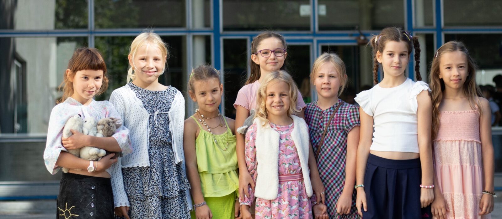 Skupina detí v slávnostnom oblečení pred budovou školy