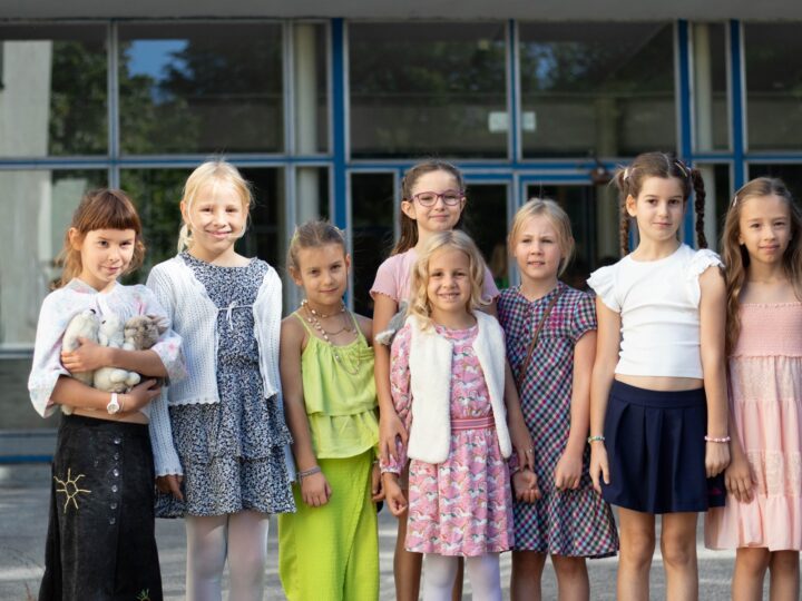 Skupina detí v slávnostnom oblečení pred budovou školy